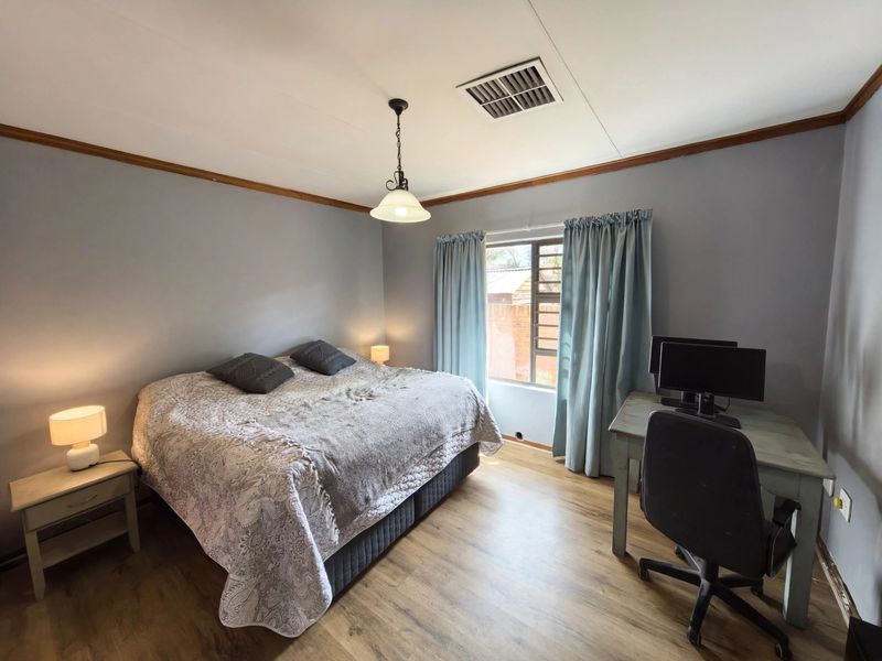 A functional bedroom featuring laminate flooring, a ceiling vent, and timber crown molding, offering a comfortable space with natural light.