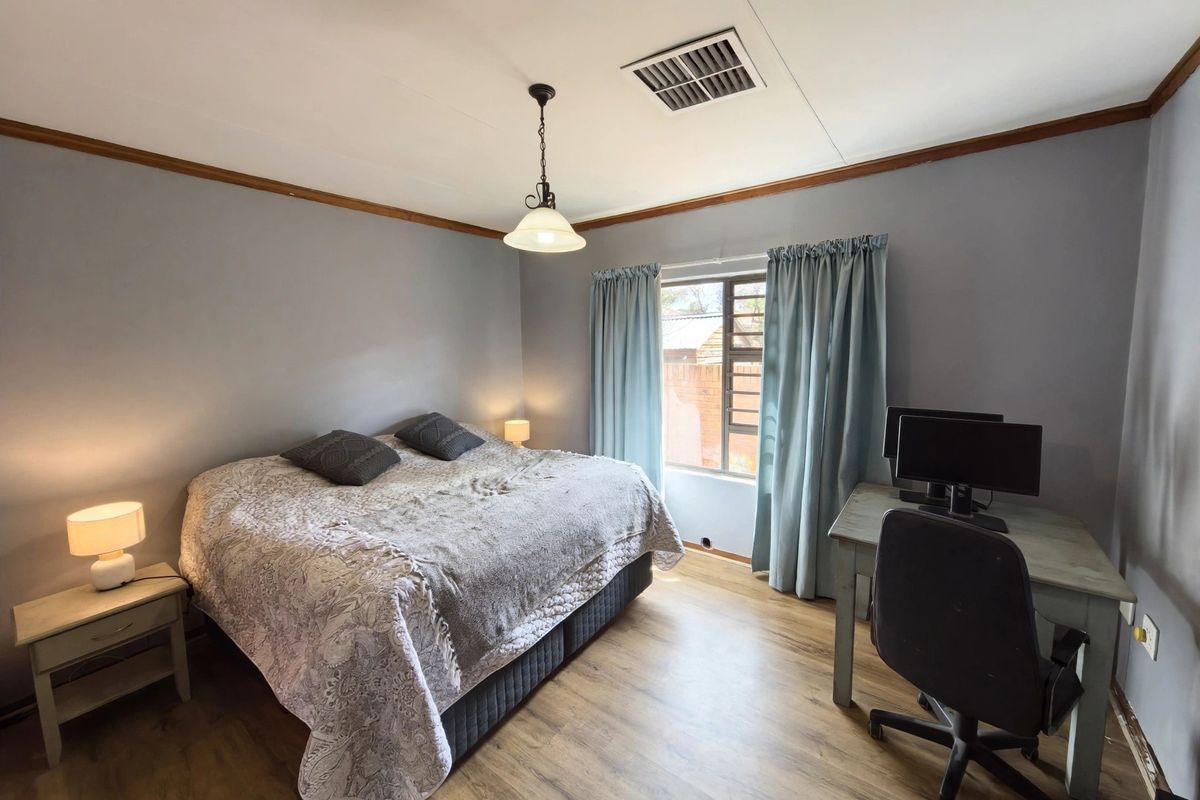 A functional bedroom featuring laminate flooring, a ceiling vent, and timber crown molding, offering a comfortable space with natural light.