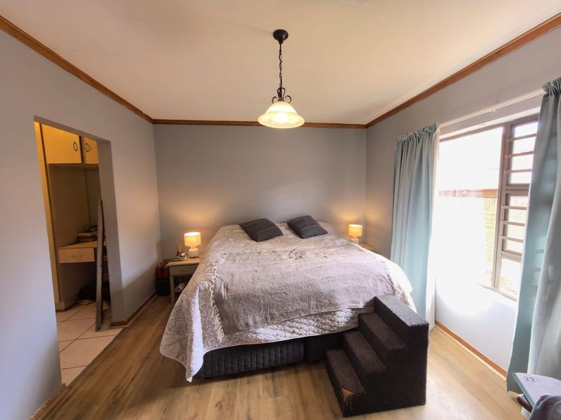 A cozy bedroom featuring laminate flooring, timber crown molding, a central pendant light, and an adjoining walk-in closet area.