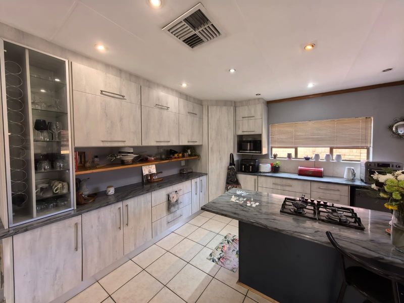 Modern kitchen featuring light wood-grain cabinetry, dark stone countertops, a central island with a gas cooktop, and ample storage space.