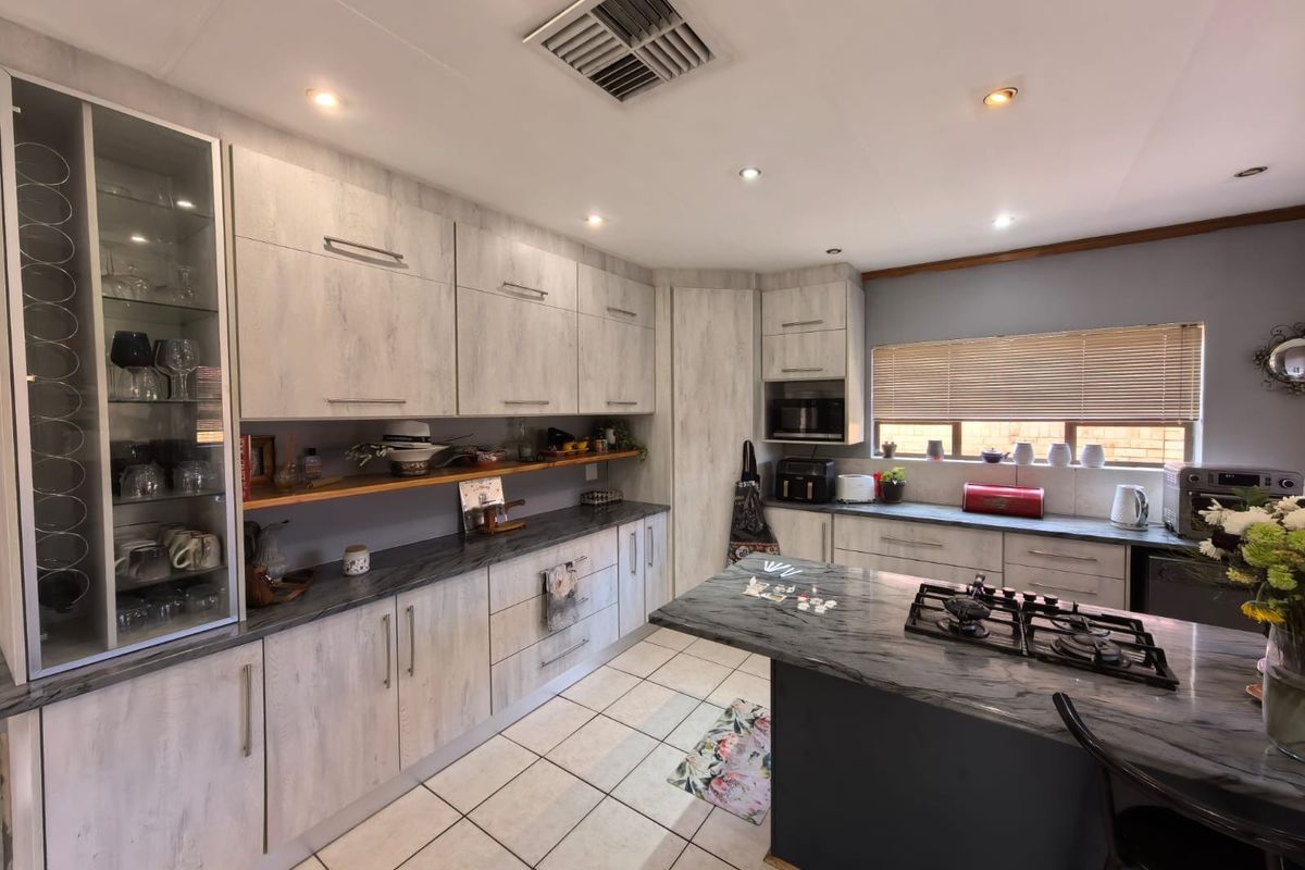 Modern kitchen featuring light wood-grain cabinetry, dark stone countertops, a central island with a gas cooktop, and ample storage space.