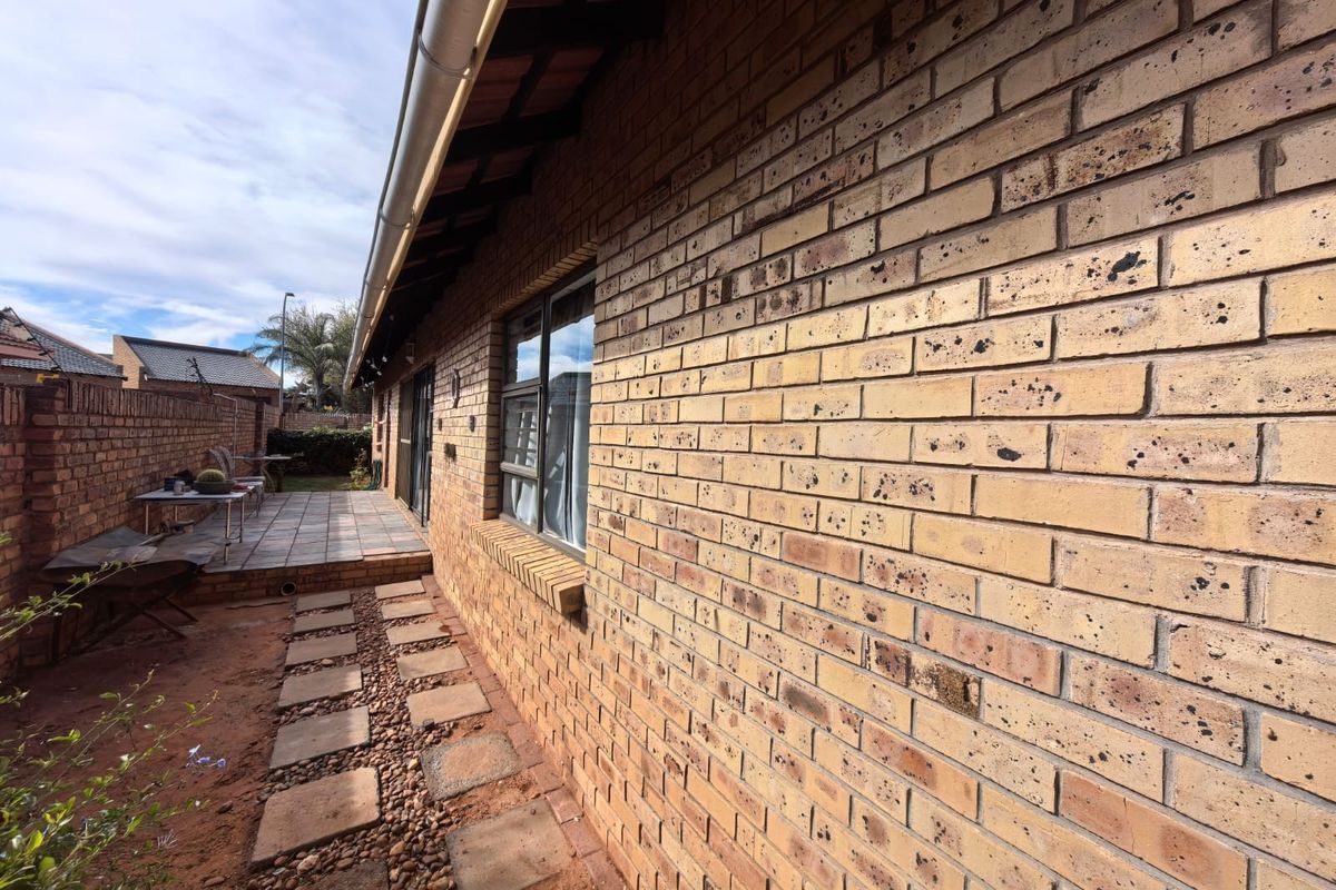 A side view of the property featuring a face brick exterior, tiled patio area, and paved walkway leading along the building.