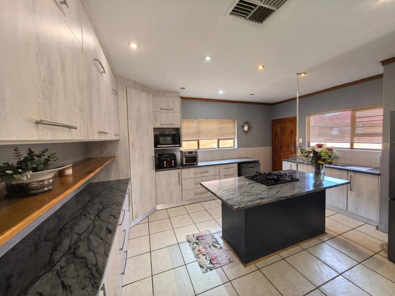 Spacious kitchen featuring a central island with a gas hob, stone countertops, ample built-in cabinetry, and tiled flooring throughout.