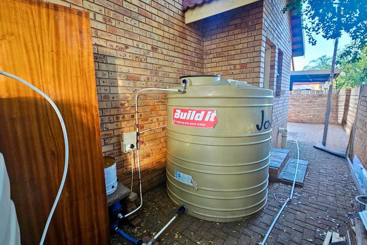 Rear exterior area featuring a water storage tank installed against a face brick wall with paved ground surface.