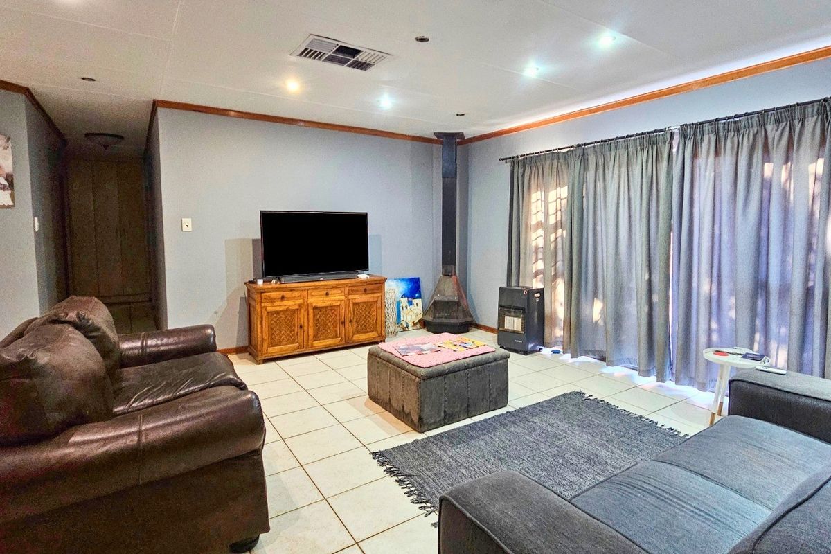 Spacious living room featuring tiled flooring, a central freestanding fireplace, recessed downlighting, and large sliding glass doors with curtains.