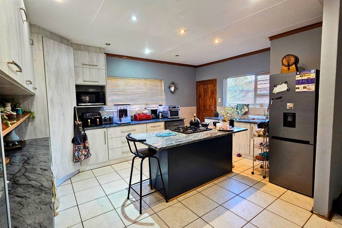 A functional kitchen featuring light wood-grain cabinetry, a central island with a gas hob, tiled flooring, and recessed lighting.