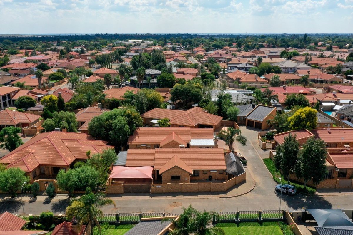 An aerial view of a residential neighbourhood featuring multiple homes with tiled roofs, paved driveways, and established garden landscaping within a suburban estate.