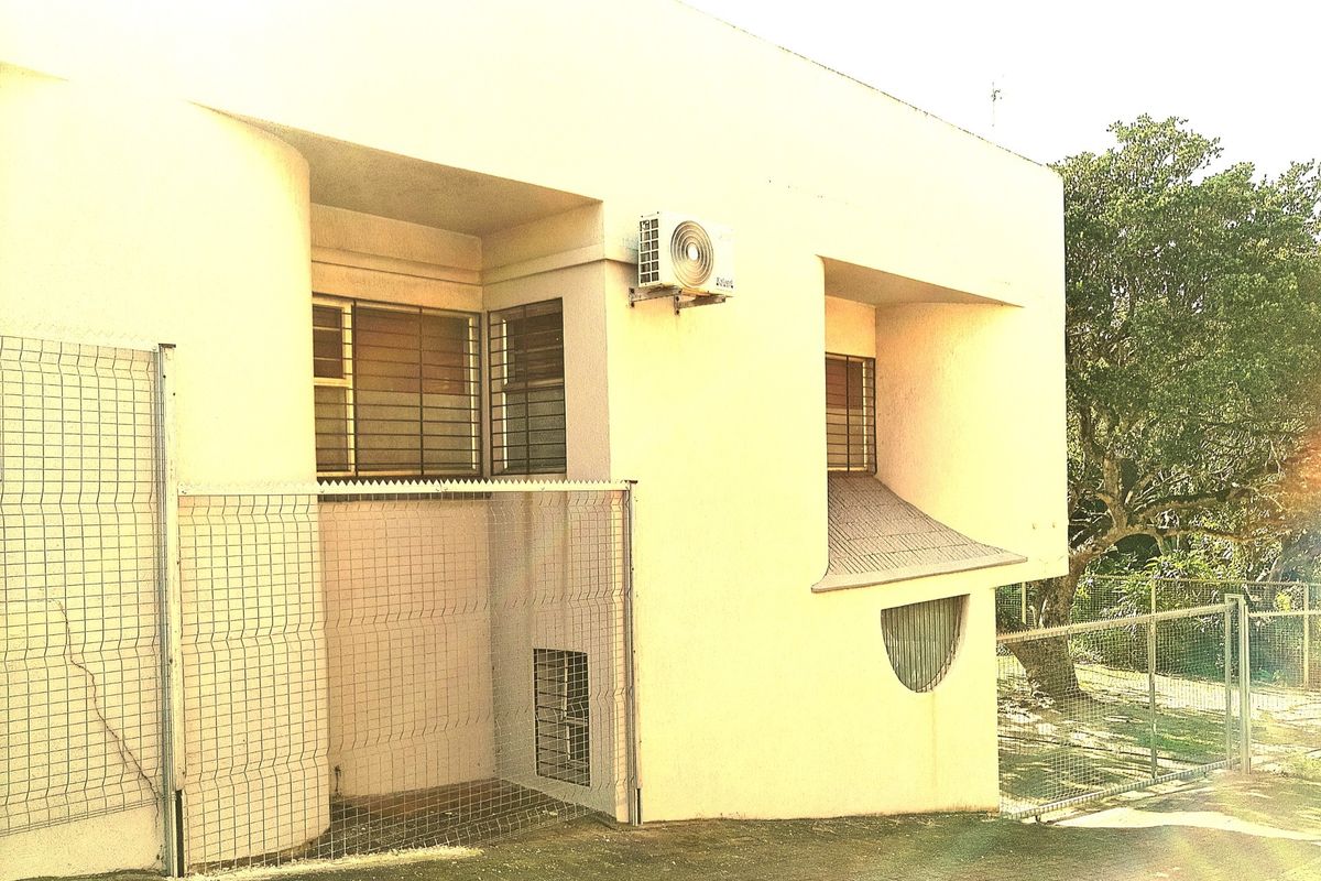 Rear exterior view of the commercial building featuring security fencing, security bars on windows, and an external air conditioning unit.