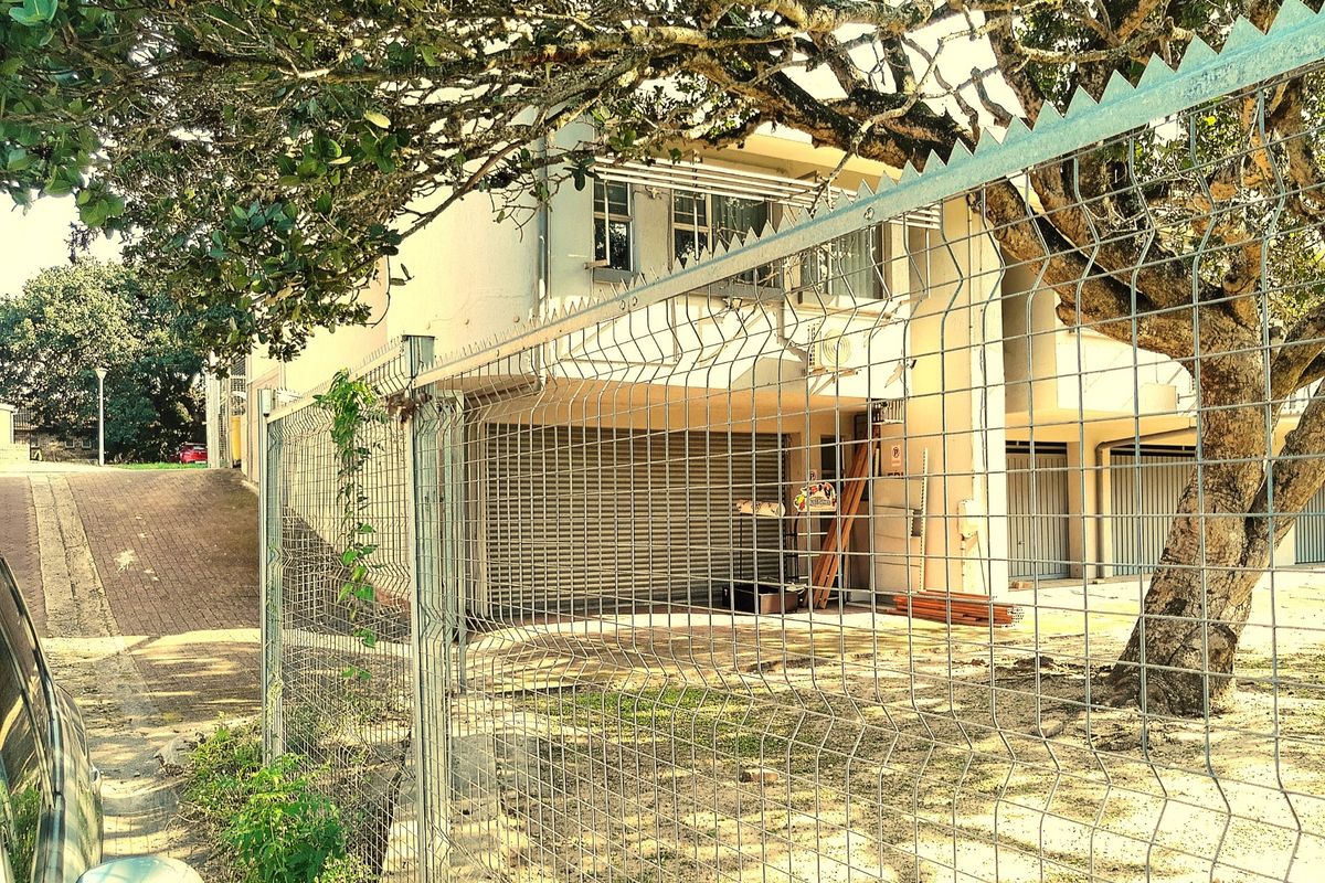 Rear exterior view of the commercial property featuring security fencing, roller shutter access, and a paved driveway area under mature trees.