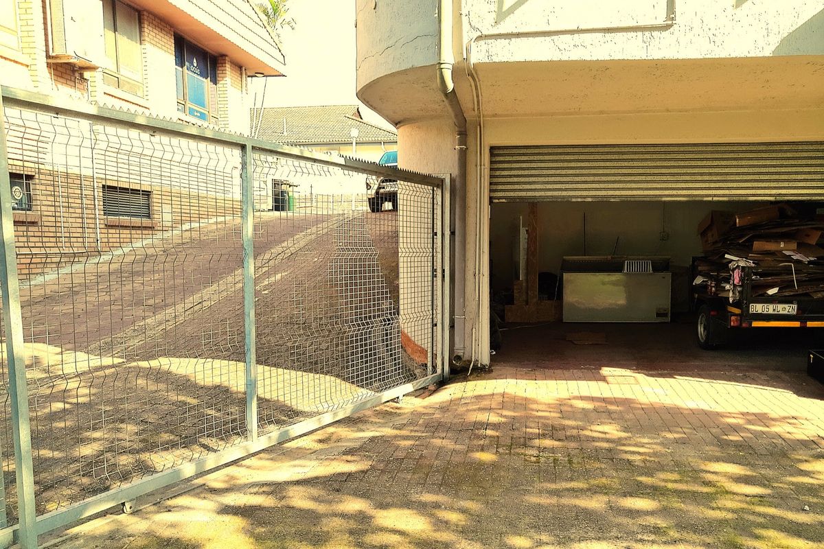 Exterior view of a commercial garage entrance featuring a roller shutter door, paved driveway, and security fencing.