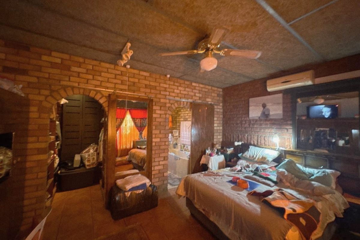 Bedroom featuring exposed brick walls, arched entryways, ceiling fan, and split system air conditioning, with direct access to an adjoining bathroom area.