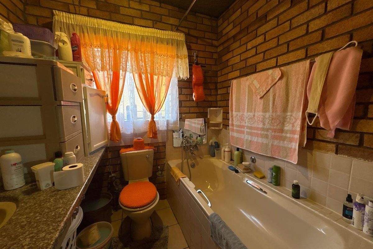 A dated bathroom featuring exposed brick walls, a built-in bathtub, and a vanity counter, offering significant potential for a modern renovation.