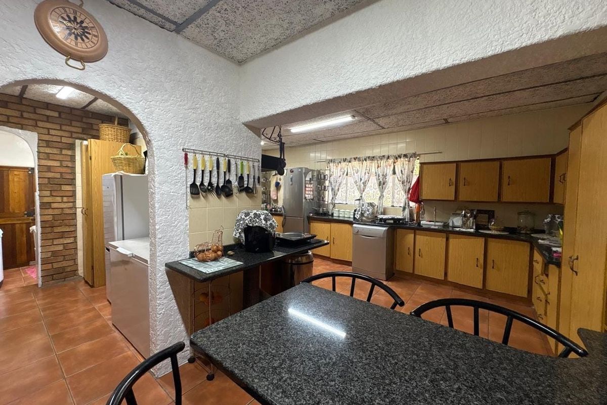 A dated kitchen featuring wood-tone cabinetry, granite-look countertops, tiled flooring, and a distinctive brick archway leading to a secondary utility area.