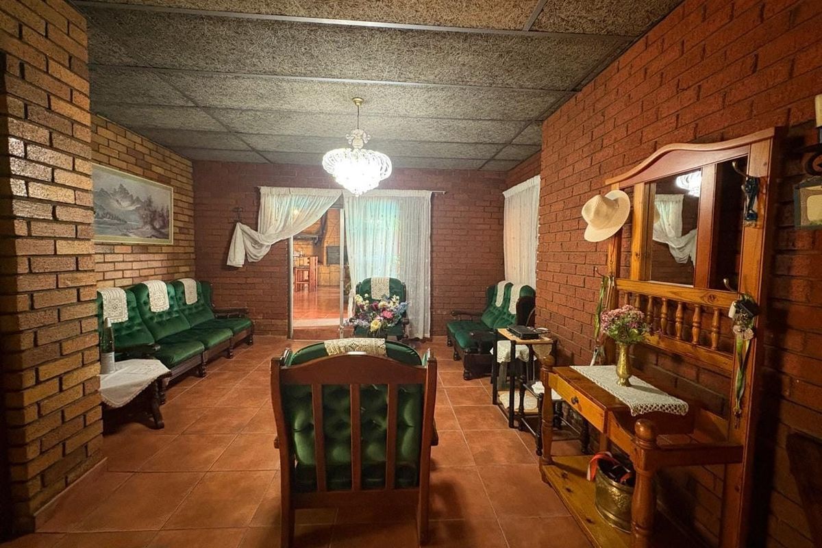 A living room featuring exposed brick walls, tiled flooring, and acoustic ceiling tiles, with a sliding glass door providing access to an adjacent space.