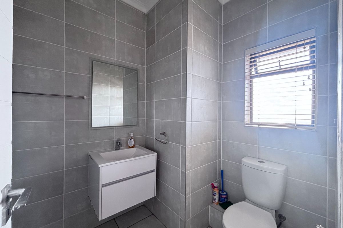 A modern, well-maintained bathroom featuring grey wall and floor tiles, a wall-mounted vanity, and a window with fitted venetian blinds.