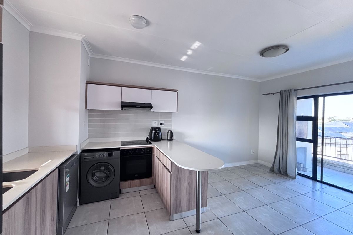 Modern open-plan kitchen and living area featuring sleek cabinetry, built-in appliances, tiled flooring, and direct access to a balcony through sliding glass doors.