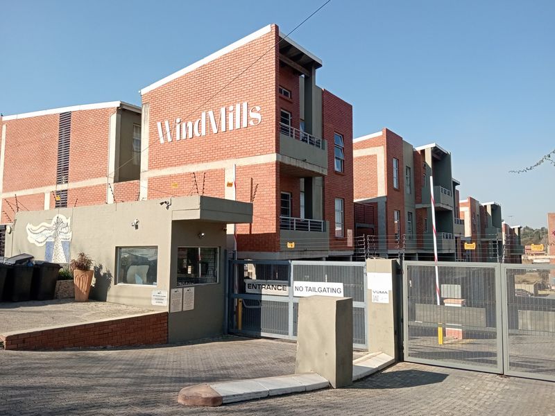 Front entrance view of the WindMills apartment complex featuring a secure gated access point, guard house, and modern brick facade architecture.
