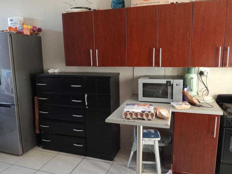 A functional kitchen area featuring wood-tone wall cabinetry, a countertop workspace, and tiled flooring, offering potential for cosmetic updates to modernize the space.