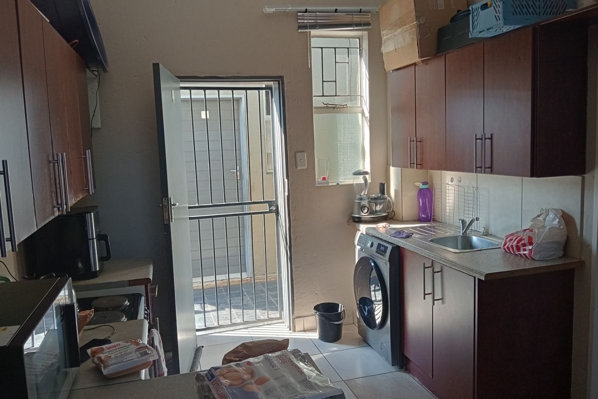 A functional kitchen featuring dark wood-finish cabinetry, laminate countertops, a stainless steel sink, and direct access to an exterior area via a security gate.