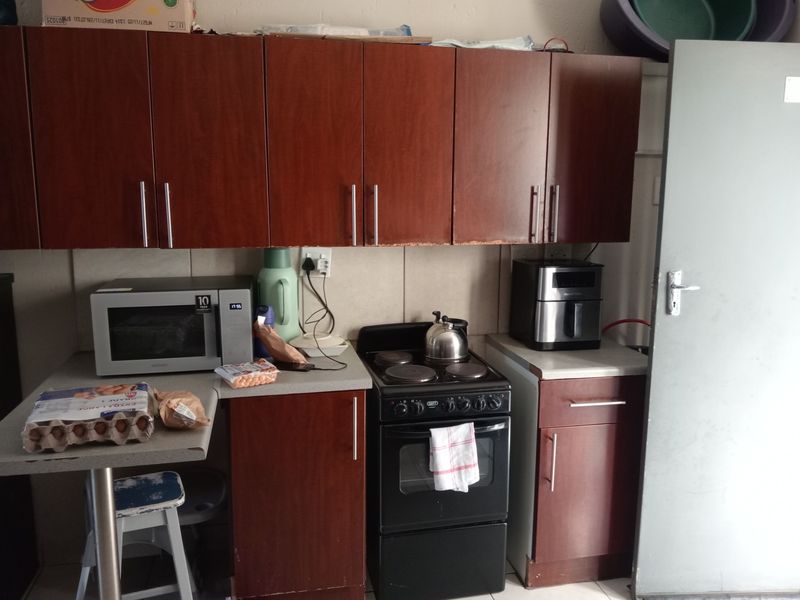 A compact kitchen featuring dark wood-look cabinetry, a freestanding electric stove, and tiled backsplash, showing signs of wear and dated finishes.