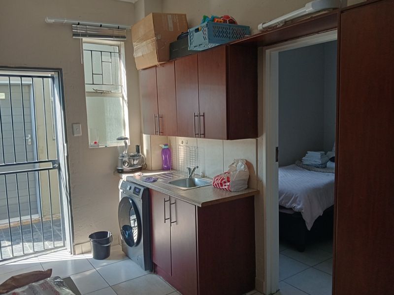 Compact kitchen area featuring built-in cabinetry, laminate countertops, and a stainless steel sink, with direct access to an adjacent bedroom and exterior entrance.