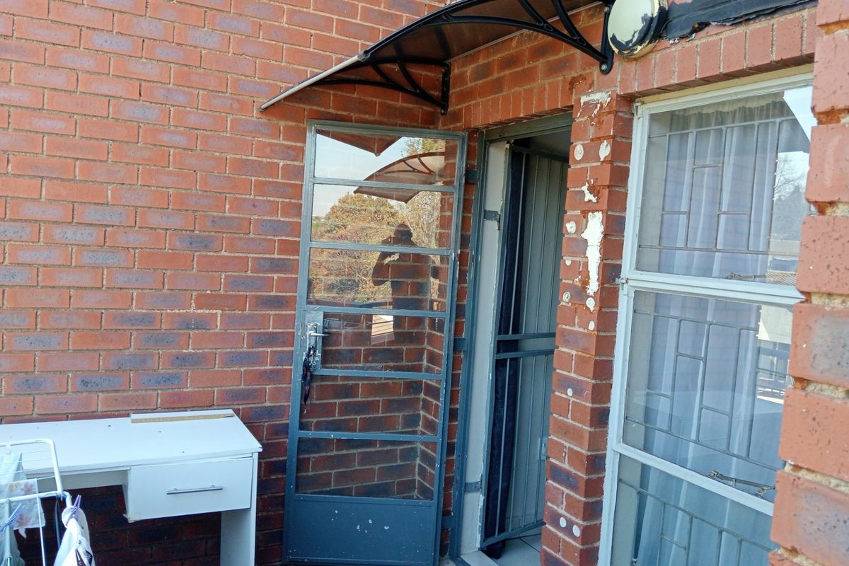 Rear exterior view of an apartment featuring a brick facade, security gate, and protective awning over the entrance.