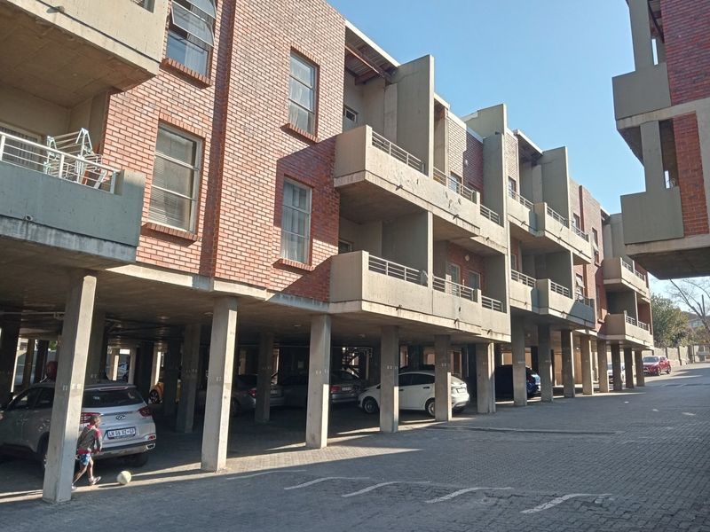 Exterior view of a multi-story apartment complex featuring exposed brickwork, concrete balconies, and a covered ground-level parking area.