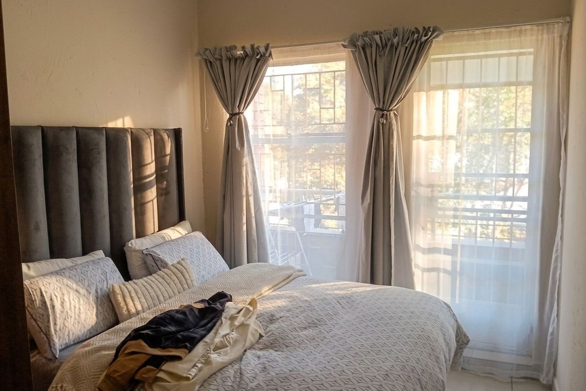 A bedroom featuring tiled flooring and windows fitted with security bars, allowing for natural light.