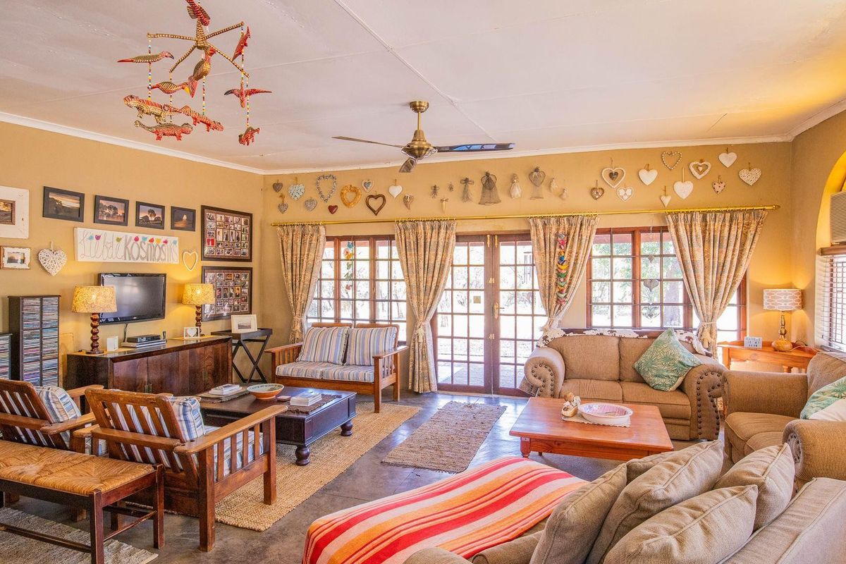 A spacious living room featuring tiled flooring, a ceiling fan, and double glass doors leading to the exterior, with an arched window and wall-mounted air conditioner.