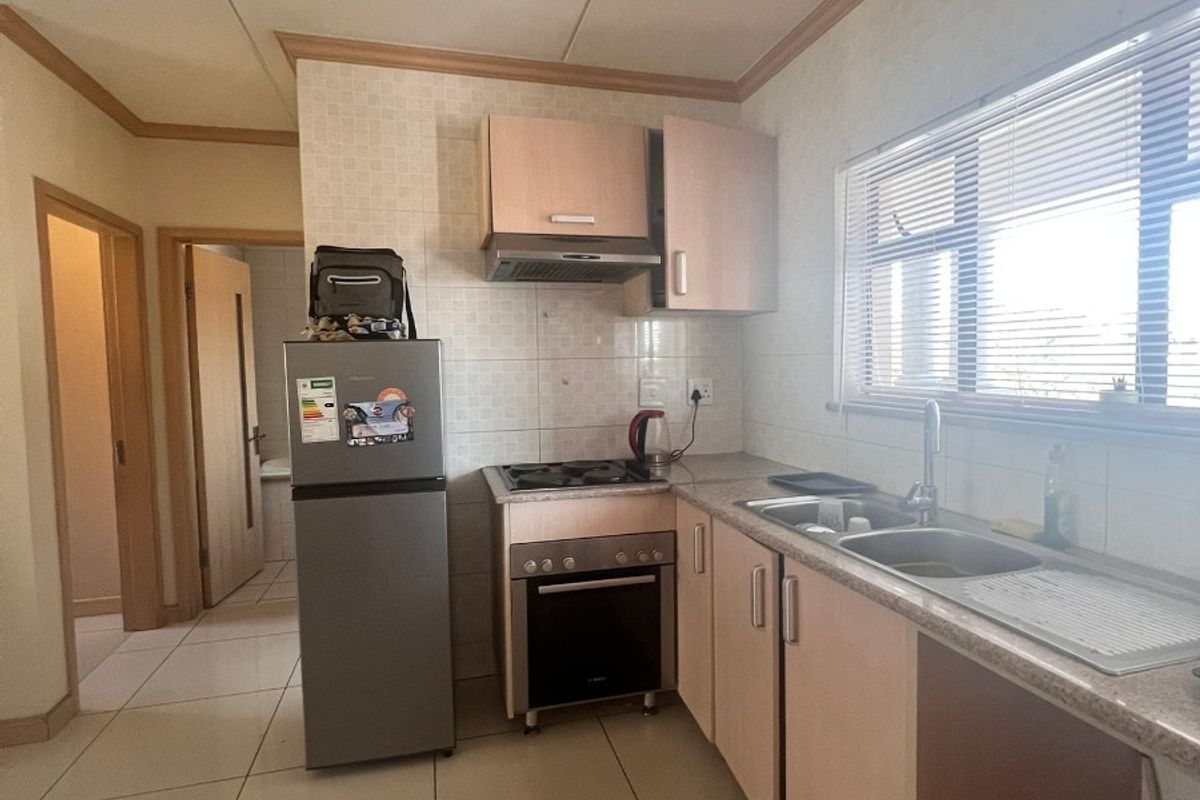 Functional kitchen featuring built-in cabinetry, gas hob, oven, extractor fan, and tiled finishes, offering a practical layout with natural light.