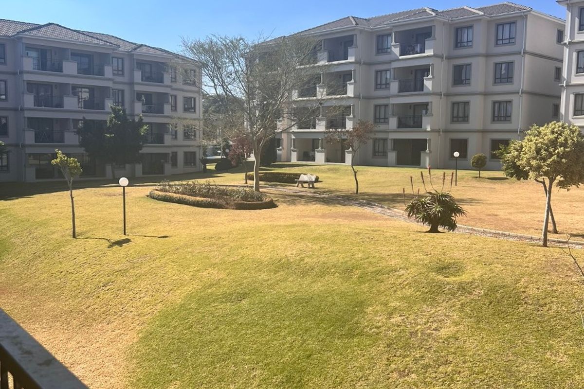 View of the well-maintained communal garden and lawn area between apartment blocks, featuring paved pathways and established landscaping.