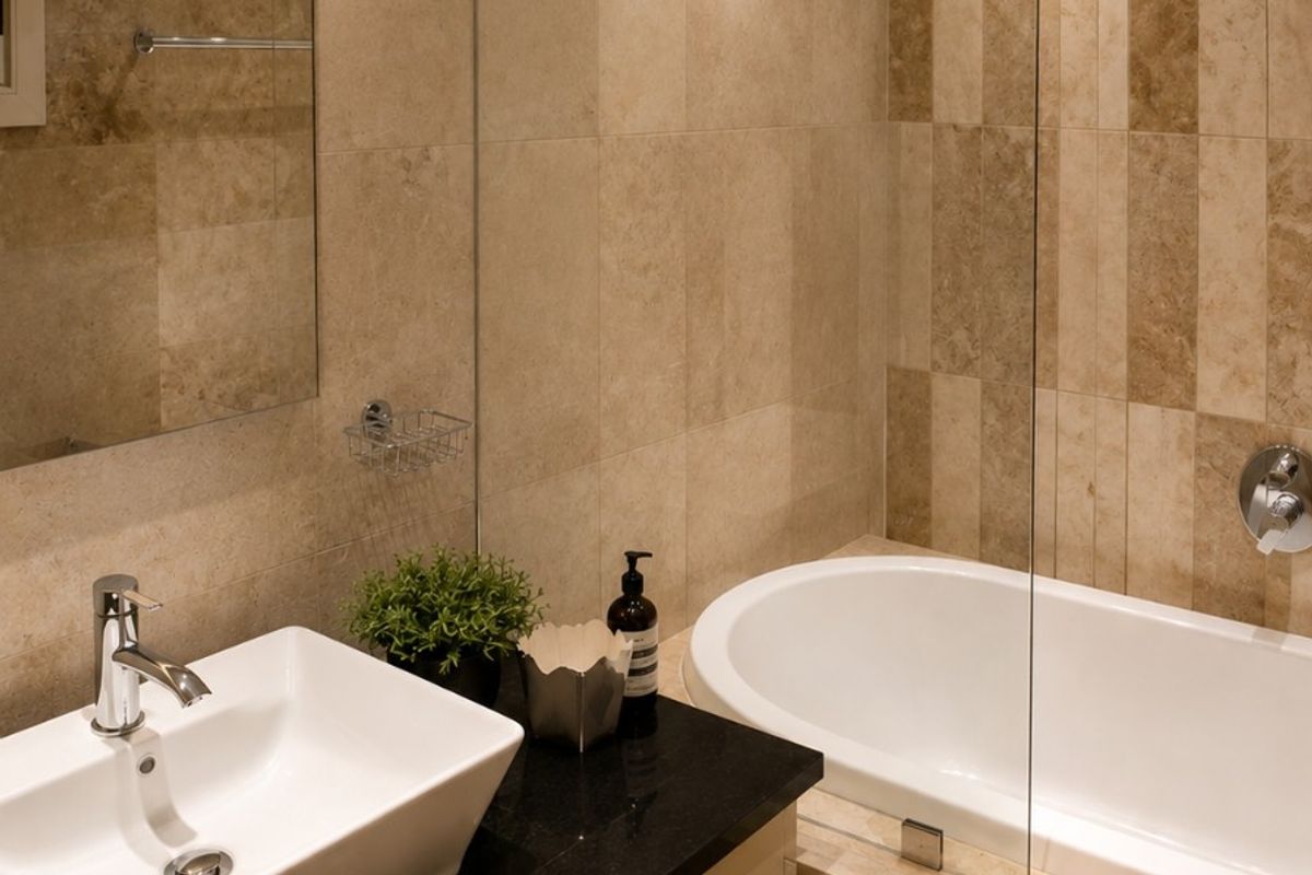 Modern bathroom featuring a vessel sink on a granite vanity, a built-in bathtub with a glass screen, and elegant stone wall tiling.