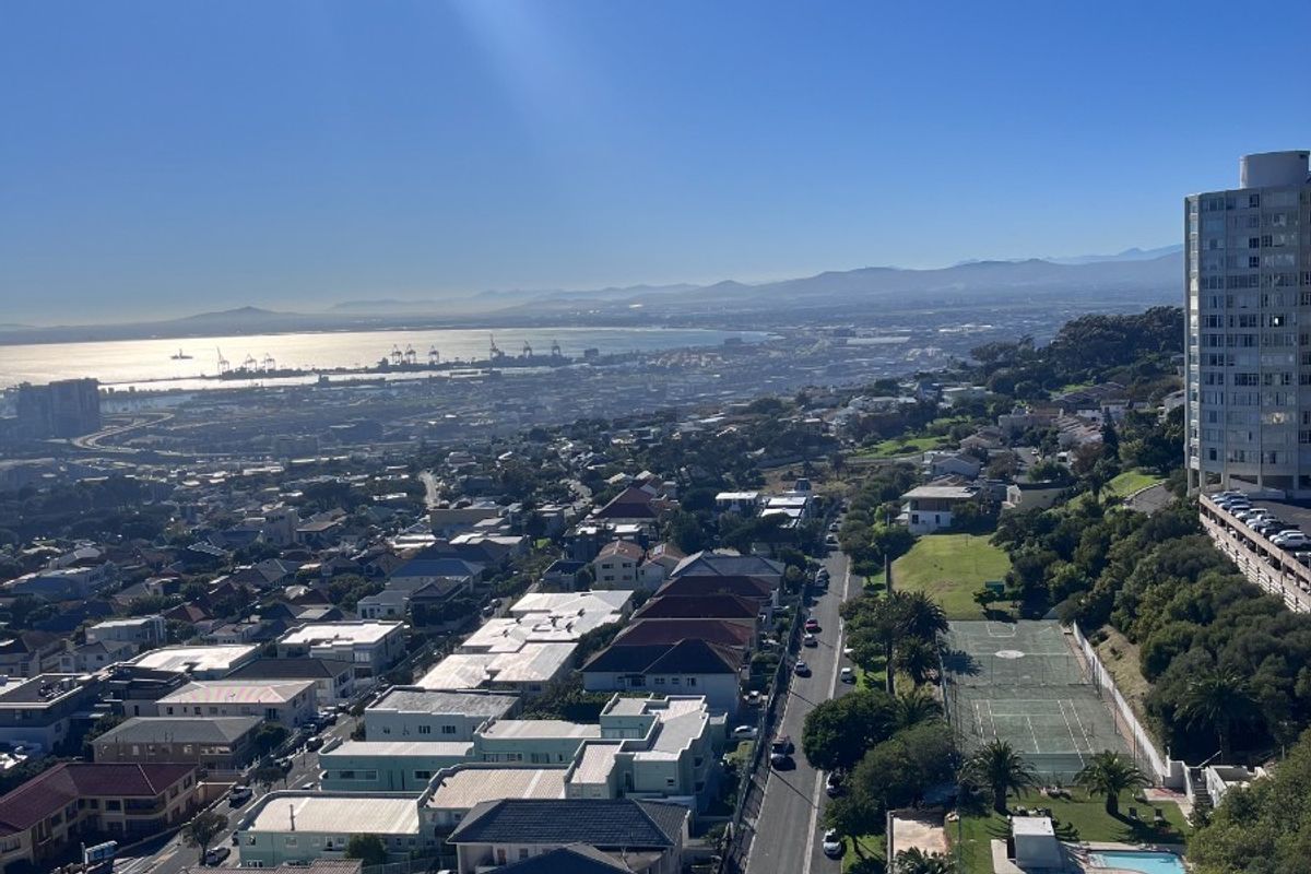 Elevated aerial view overlooking the surrounding residential neighborhood, coastal landscape, and shared complex amenities including a swimming pool and tennis court.