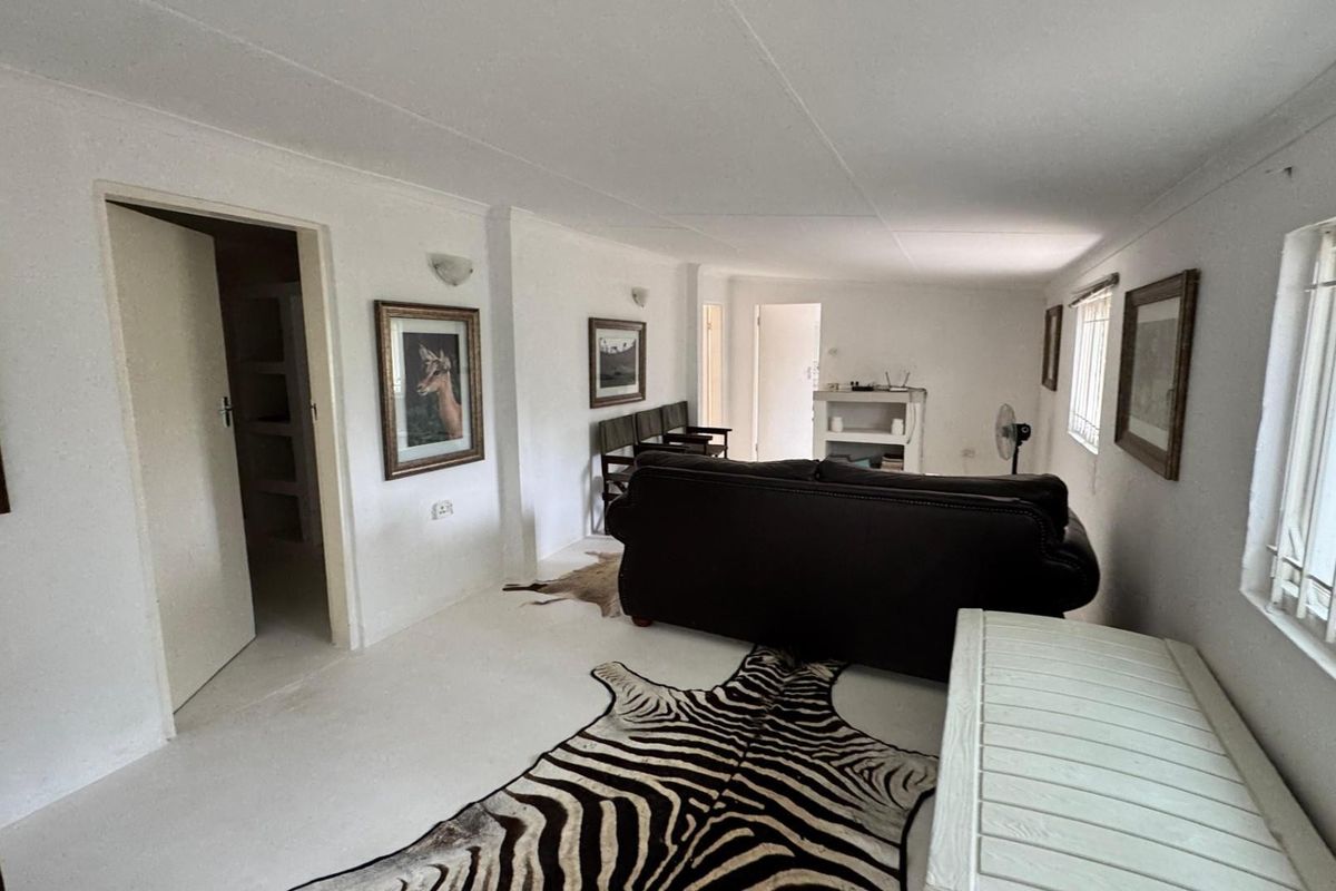 A living room area featuring white walls, tiled flooring, and security bars on the windows, providing a functional and neutral space.