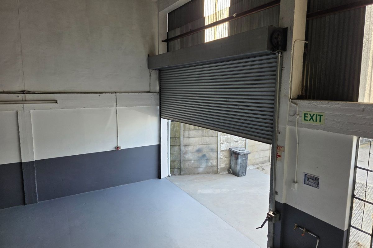 Industrial utility space featuring a high-clearance roller shutter door, concrete flooring, and exposed structural elements, suitable for storage or workshop operations.