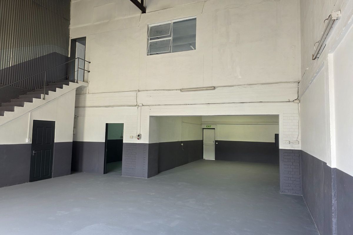 Spacious industrial utility area featuring high ceilings, concrete flooring, and a staircase leading to an upper level, suitable for storage or workshop use.