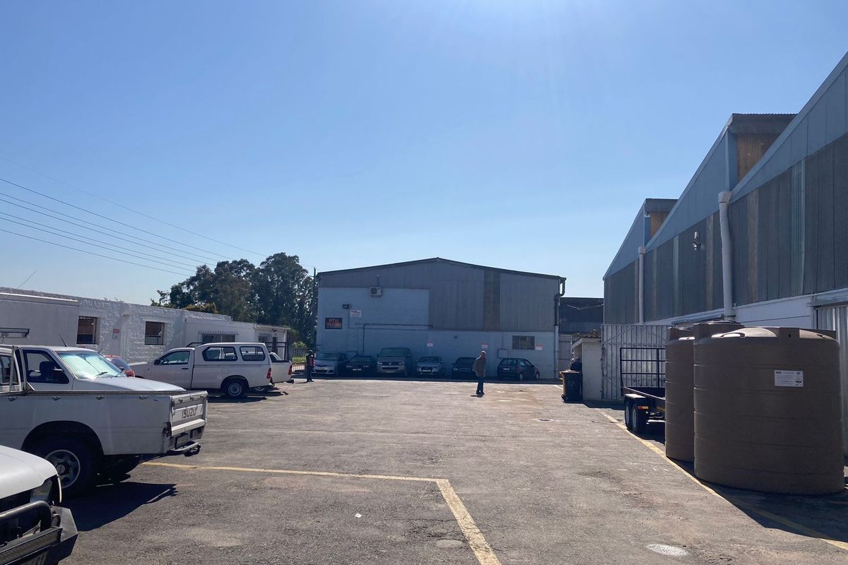 Industrial yard area featuring asphalt paving, corrugated metal building facades, and large water storage tanks.