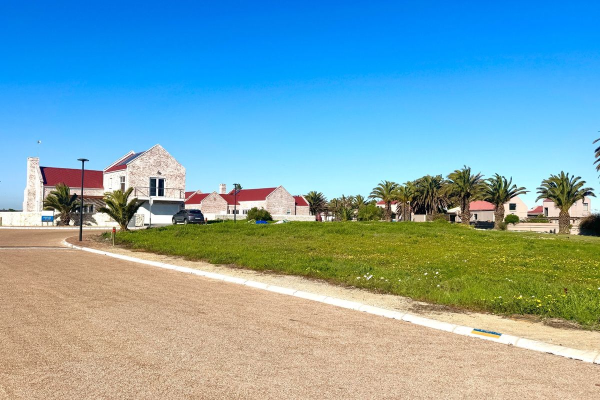A street-level view of a residential vacant land plot featuring paved road access, concrete curbing, and established surrounding residential properties.