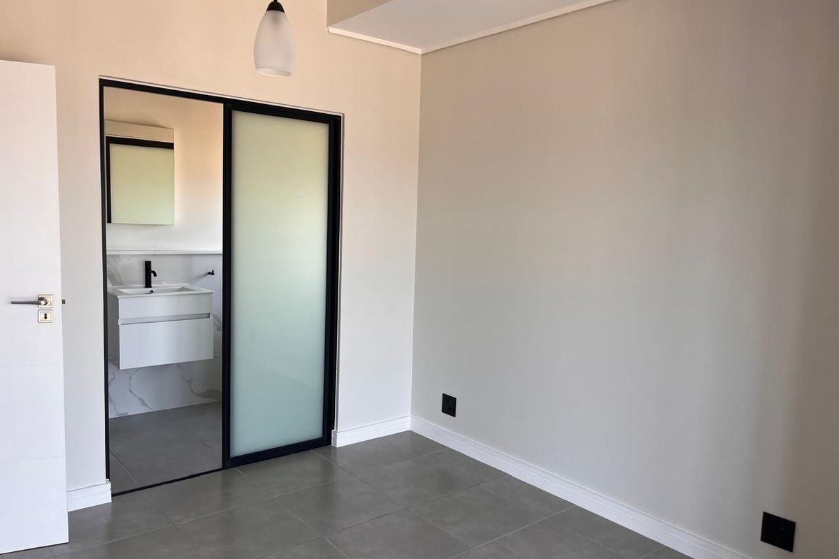 A modern, empty bedroom featuring neutral walls, tiled flooring, and a sleek sliding door leading to an en-suite bathroom.