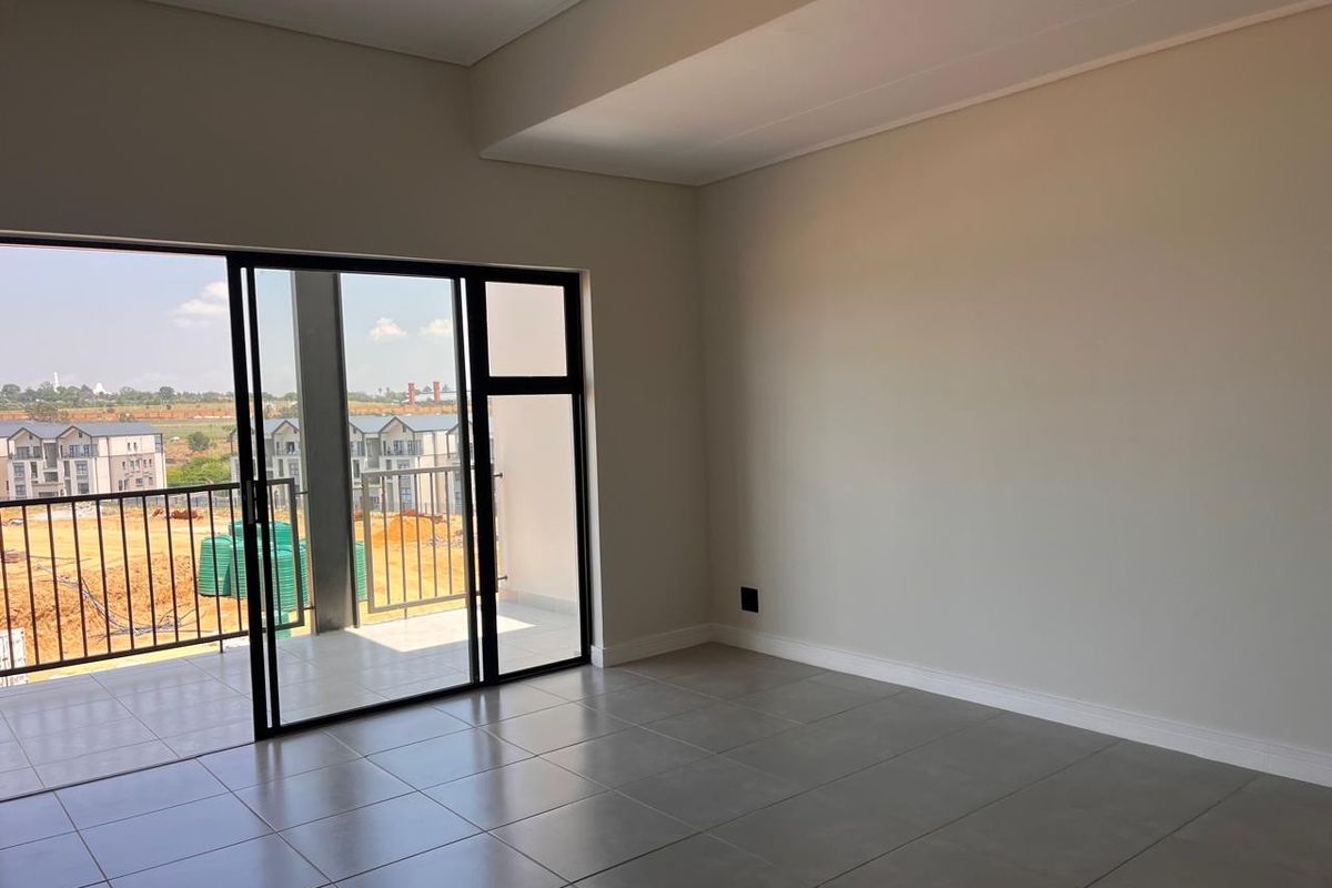 An empty, modern living area featuring neutral tiled floors and large sliding glass doors that open onto a private balcony.