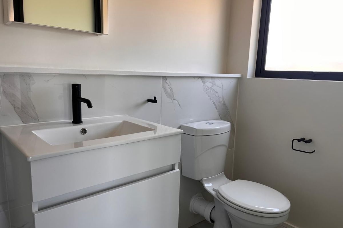 Modern bathroom featuring a sleek white vanity with black mixer tap, marble-look splashback, and contemporary toilet suite.
