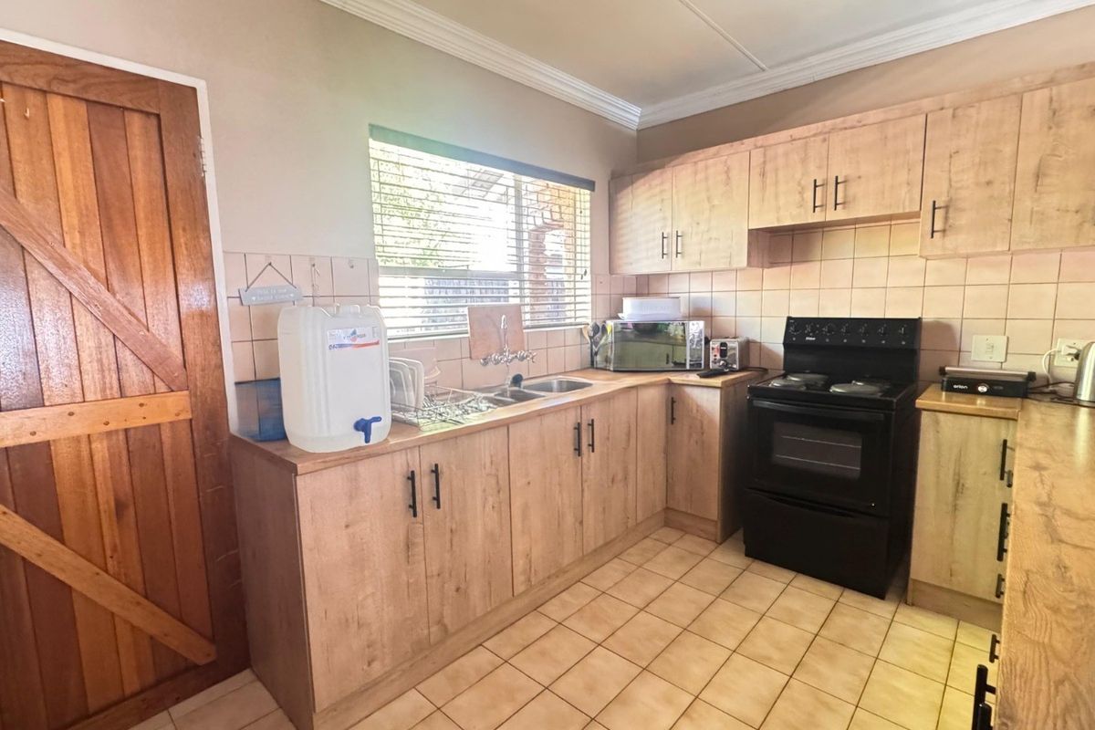 A functional kitchen featuring light wood-look cabinetry, tiled backsplash, double sink, and tiled flooring, offering a practical layout for daily meal preparation.