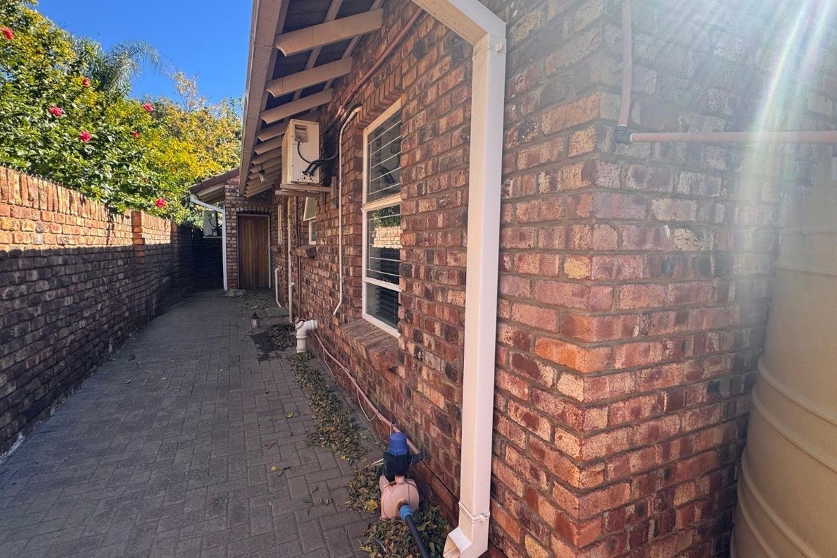 A side exterior view of the townhouse featuring a brick facade, paved walkway, boundary wall, and a water tank.