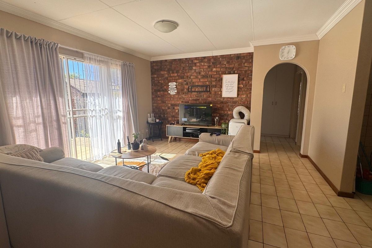 Spacious living room featuring an exposed brick accent wall, tiled flooring, and a sliding glass door providing access to the outdoor area.