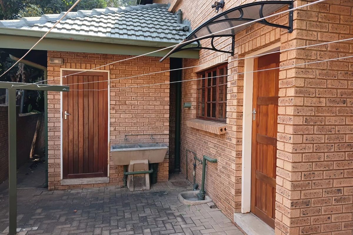 A functional rear courtyard area featuring a brick facade, timber doors, and a built-in concrete laundry trough with external plumbing.