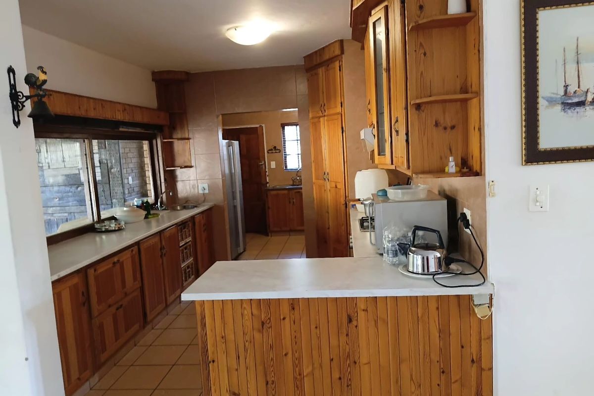 A functional kitchen featuring extensive wooden cabinetry, tiled flooring, and a breakfast bar, offering a traditional layout with a connected scullery area.