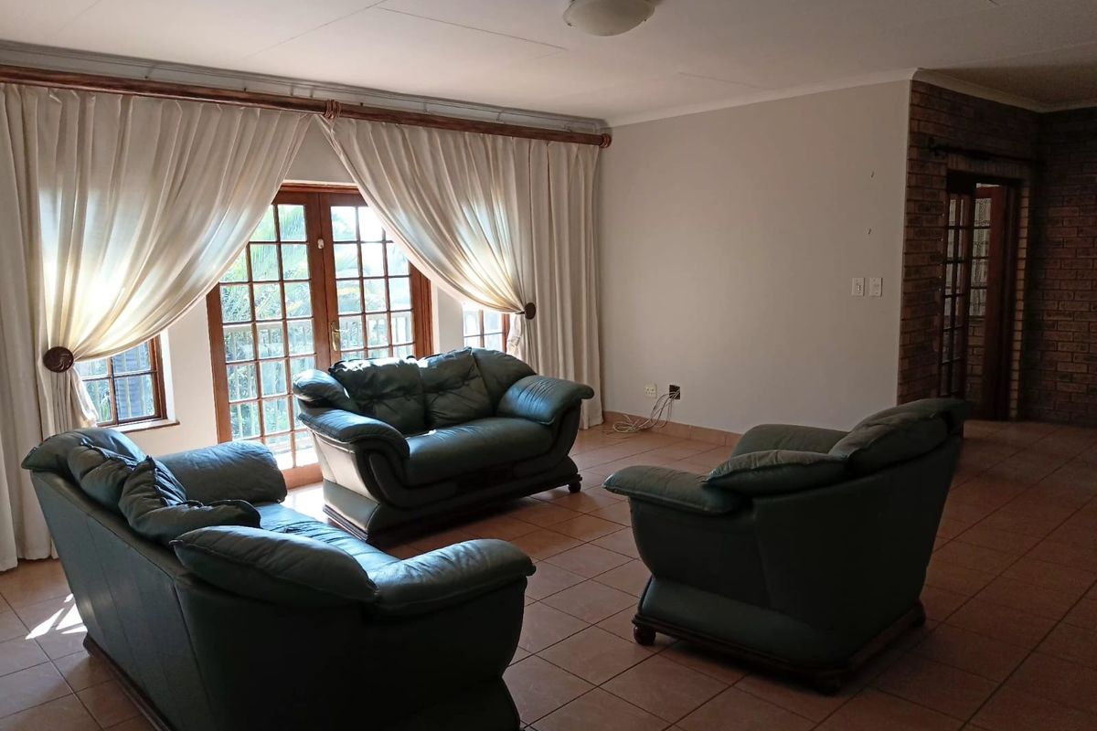 Spacious living room featuring tiled flooring, an exposed brick accent wall, and large french doors providing natural light and garden access.