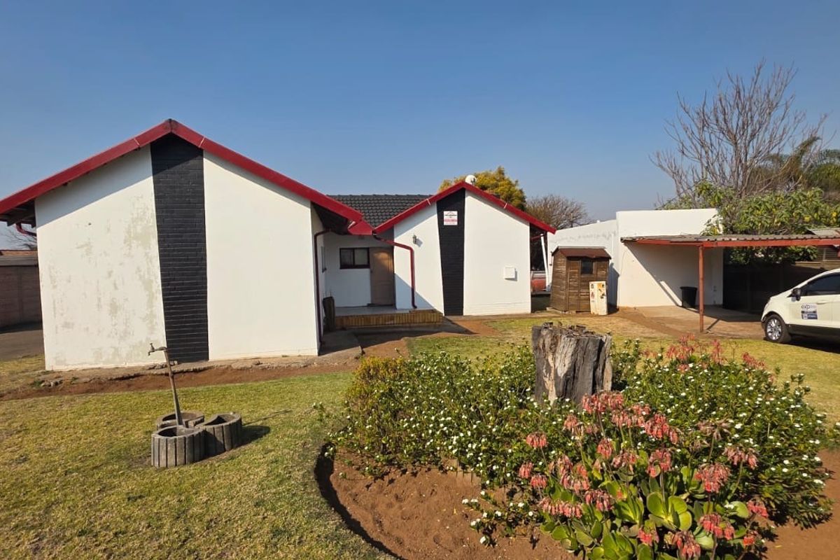 Rear view of the property featuring a metal roof, carport, and established garden area with a paved driveway.