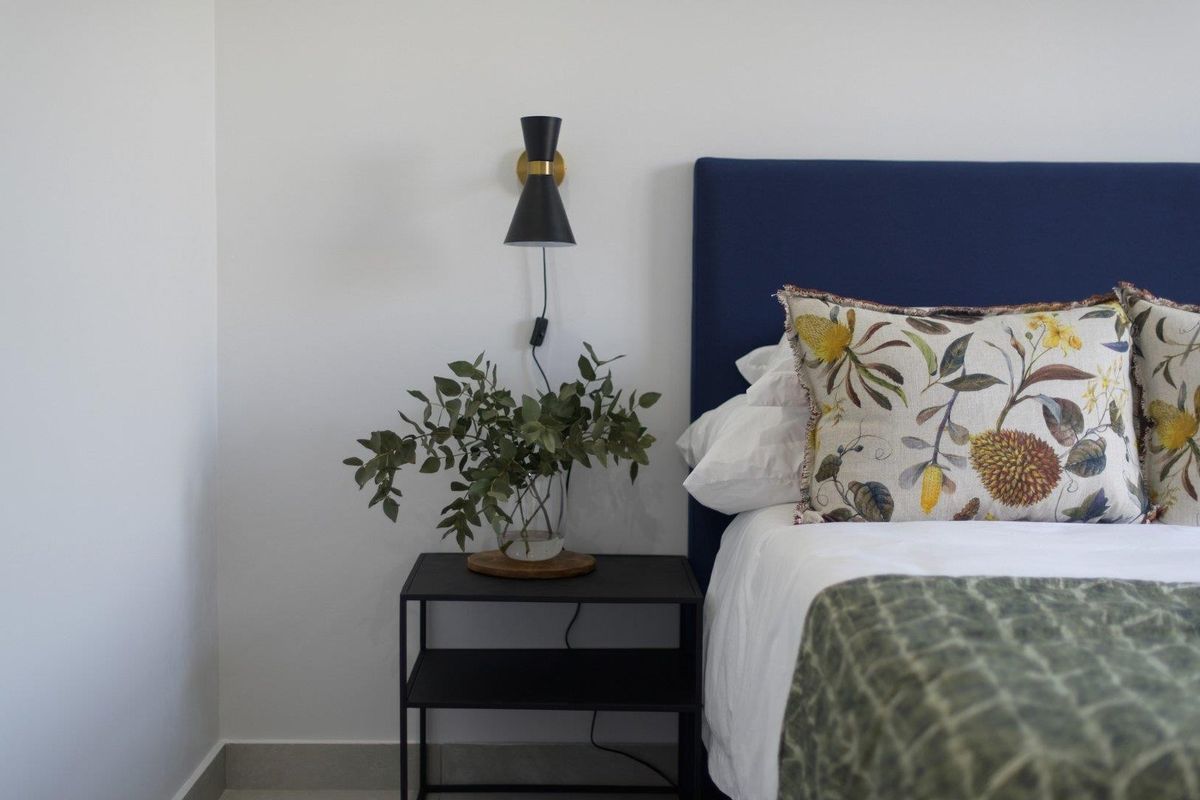 A close-up view of a bedroom corner featuring a modern wall-mounted light fixture and neutral wall finishes.