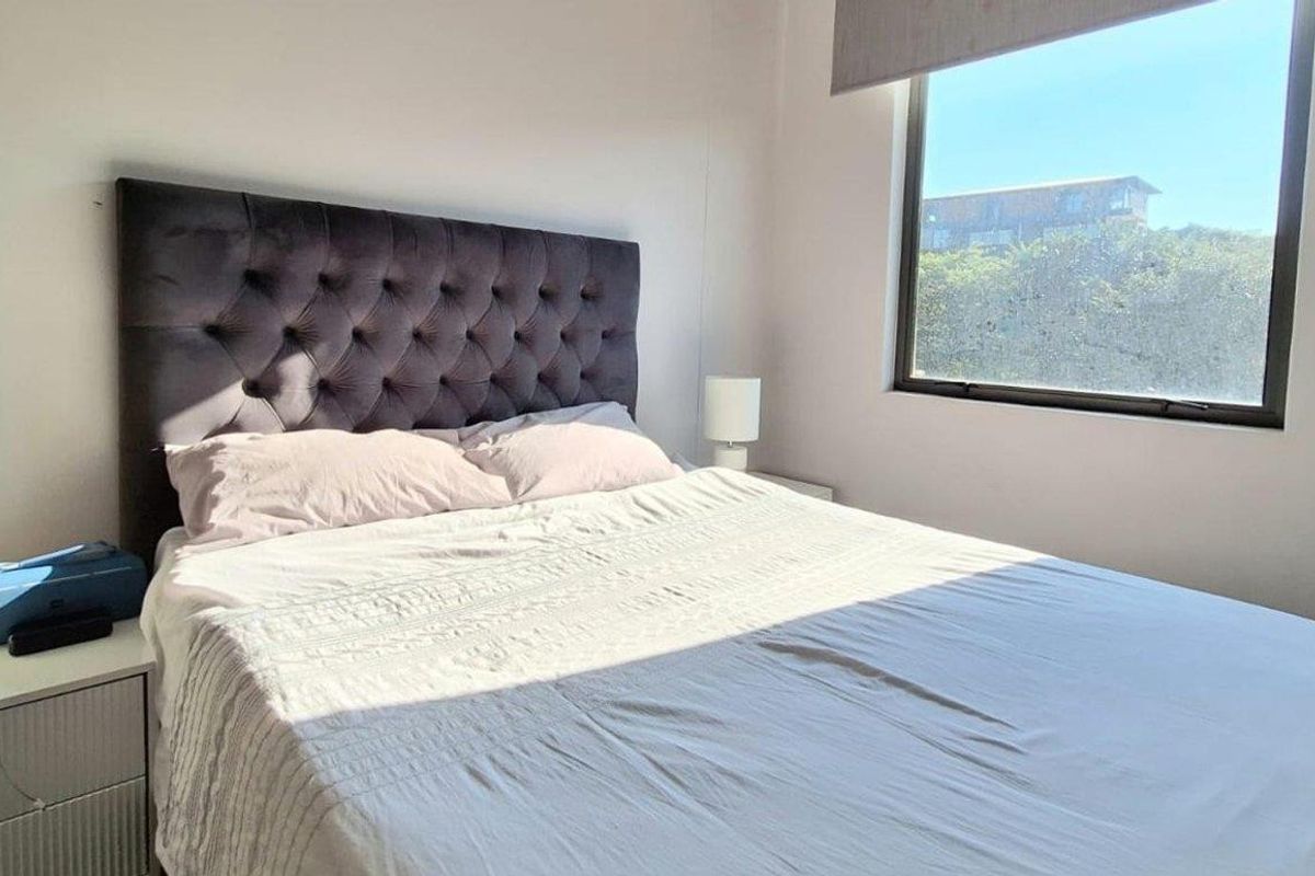 A bright bedroom featuring a large window with a roller blind, providing natural light and exterior views.